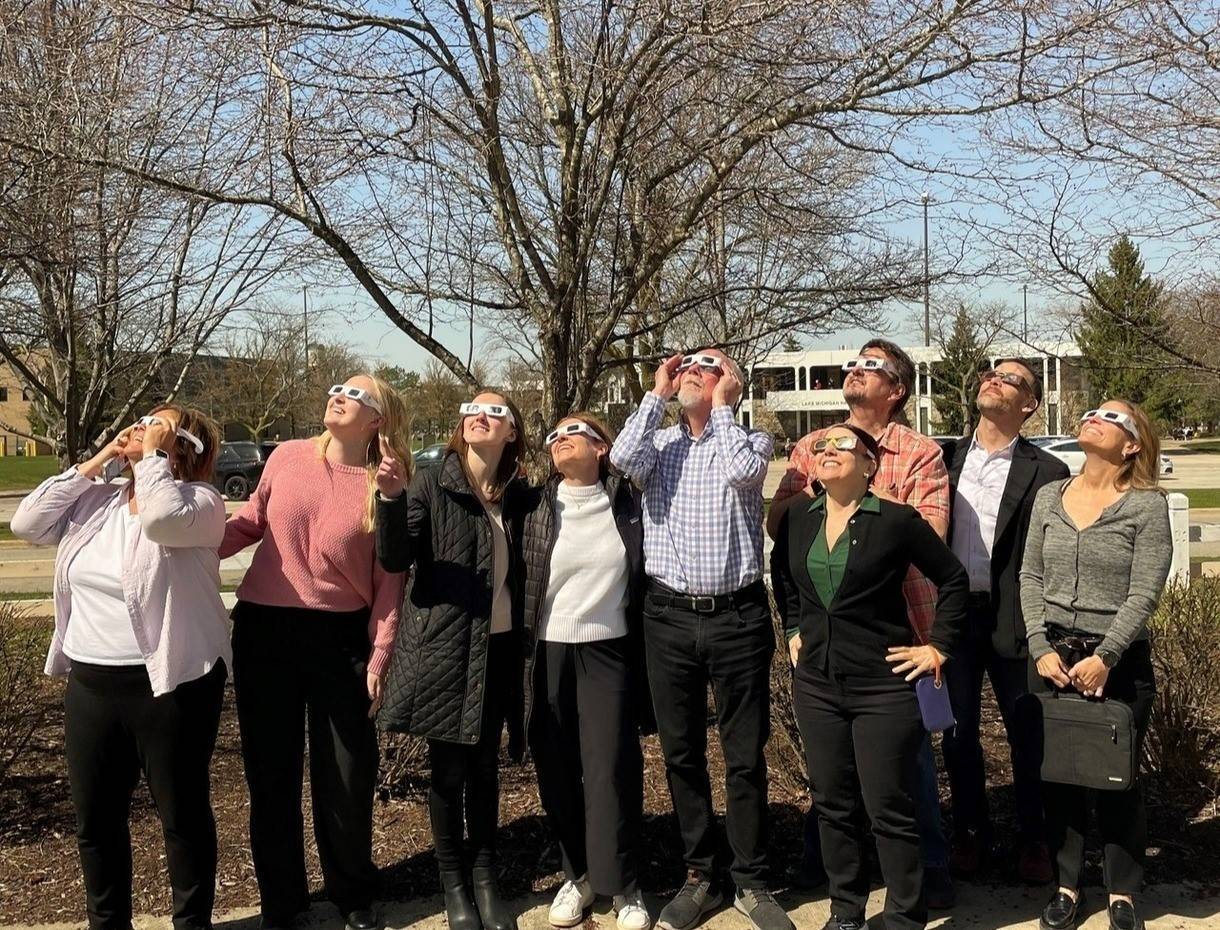 a group of faculty and staff wearing eclipse glasses to look at the eclipse